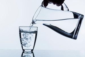 pure water is emptied into a glass of water from a jug. fresh dr