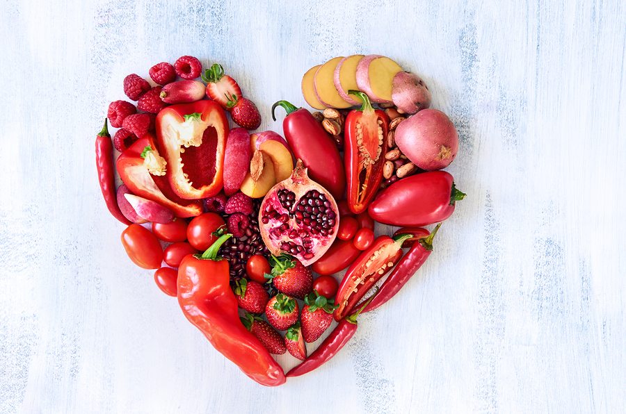 Collection of fresh red vegetables and fruits arranged in a heart shape on white rustic background strawberry raspberry pomegranate peppers capsicum chilli potato beans legumes